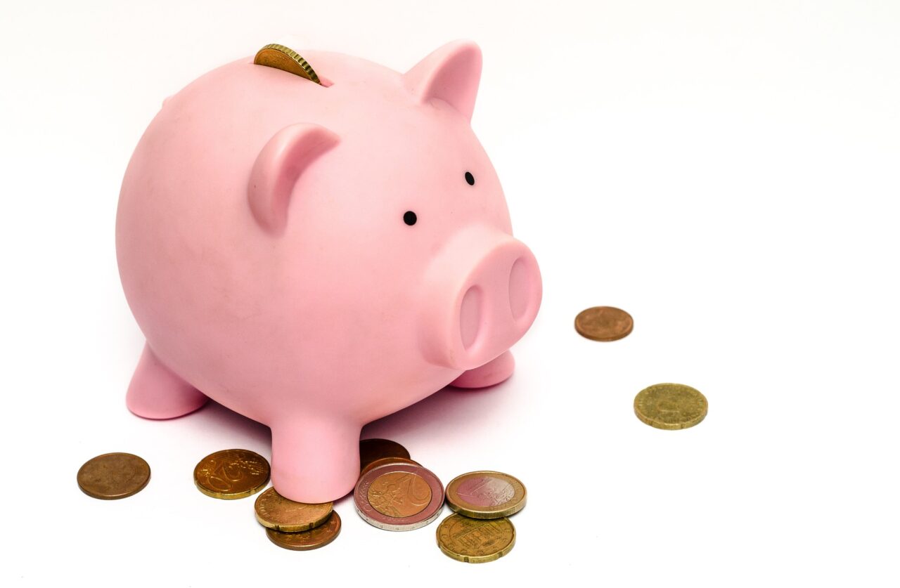 Image of a pink piggy bank with a coin halfway out of the coin slot and other coins around the piggy bank.