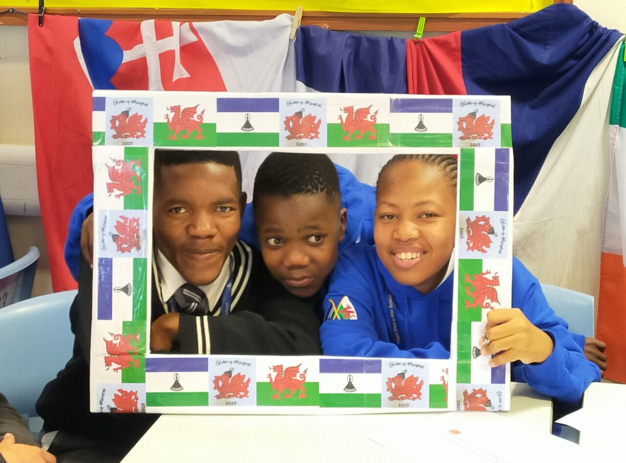 Three young people looking through a frame decorated with Welsh and Lesotho flags