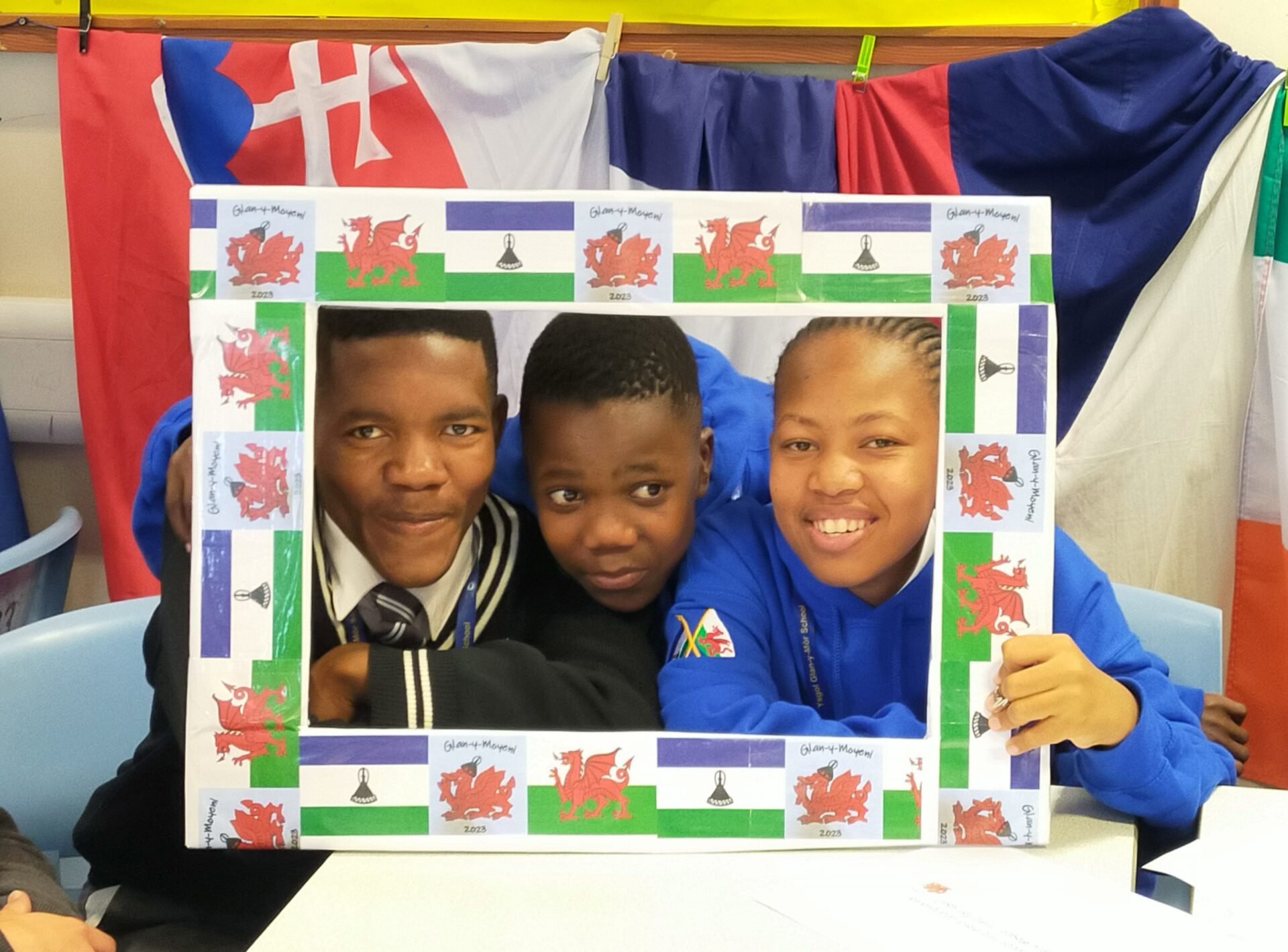 Three young people looking through a frame decorated with Welsh and Lesotho flags