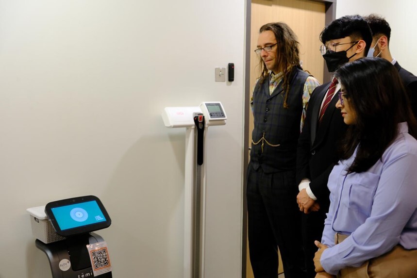 Pedwar o bobl yn edrych ar ddarn o offer. Mae dau berson yn gwisgo mwgwd wyneb.