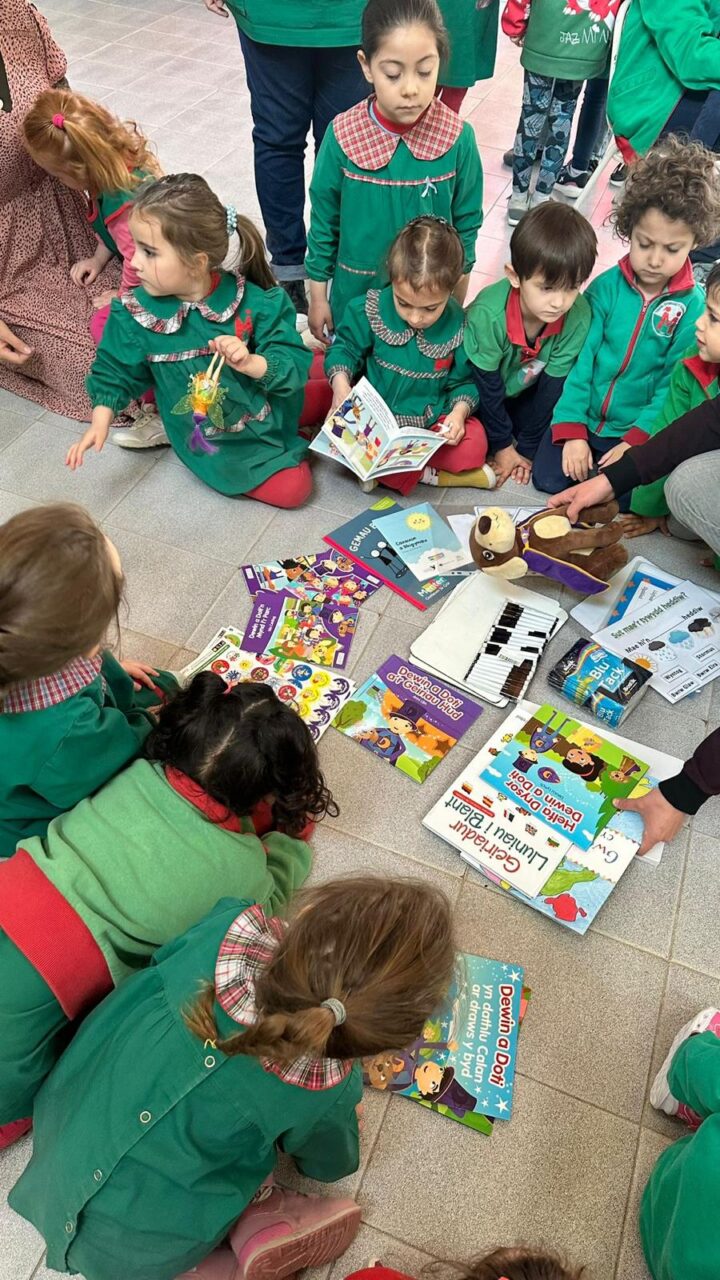 Golygfa oddi uchod o griw o blant ifanc mewn gwisg ysgol yn edrych trwy lyfrau ar y llawr. / A birdseye view of a group of young children in a uniform looking through books on the floor