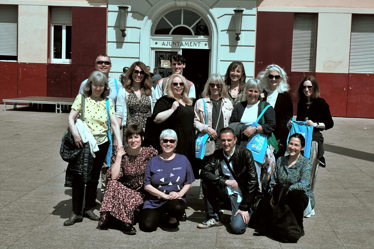 Grŵp o oedolion yn sefyll am lun yn yr haul y tu allan i adeilad coch a gwyn / A group of adults posing for a photo in the sun outside a red and white building