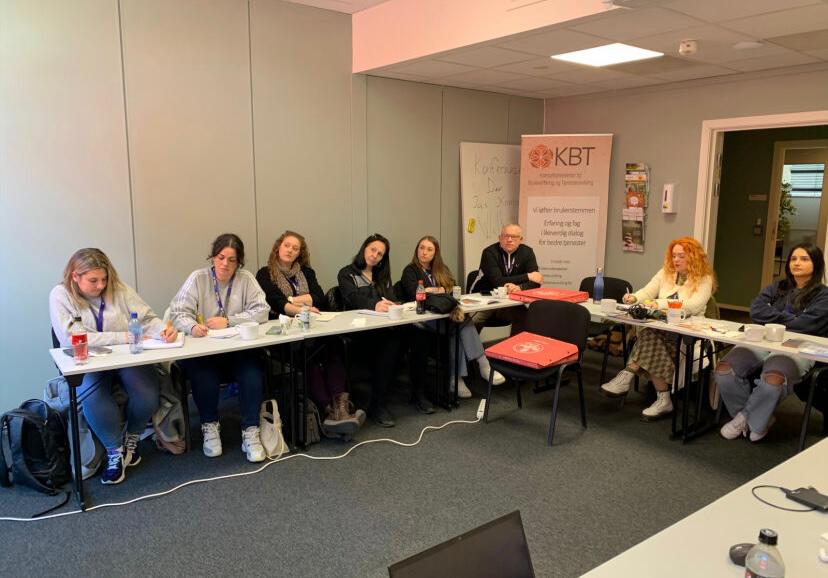 Wyth o bobl yn eistedd o amgylch bwrdd cynhadledd siâp U yn edrych ar gyflwyniad nad yw i'w weld yn y llun. / Eight people sat around a U shaped conference table looking at a presentation which isn't visible in the photo.