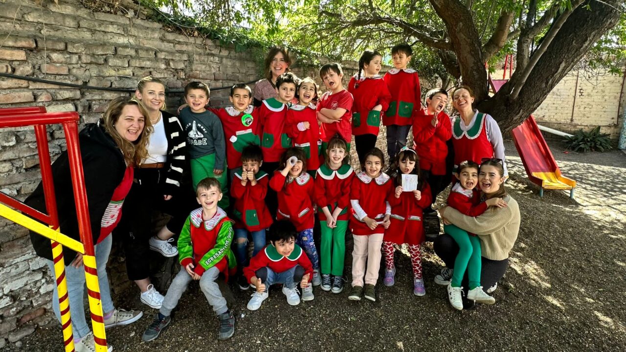Grŵp o blant ifanc mewn gwisg ysgol yn sefyll am lun gyda phump o ferched. Maen nhw y tu allan o dan goeden. / A group of young children in a uniform top posing for a photo with five women. They are outside under a tree.