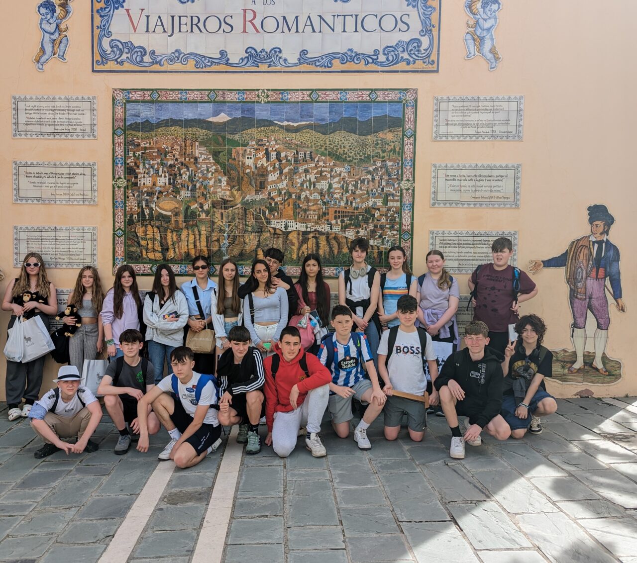 Grŵp o ddisgyblion Sbaenaidd a Chymreig yn sefyll gyda'i gilydd y tu allan o flaen murlun