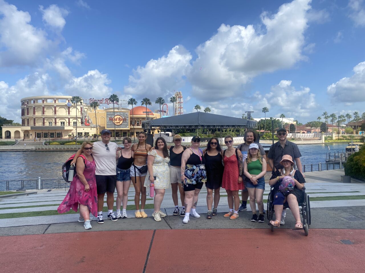 Myfyrwyr a staff PCYDDS yn sefyll am lun o flaen llyn gyda Hard Rock Café yn y cefndir. Mae un o'r myfyrwyr mewn cadair olwyn.