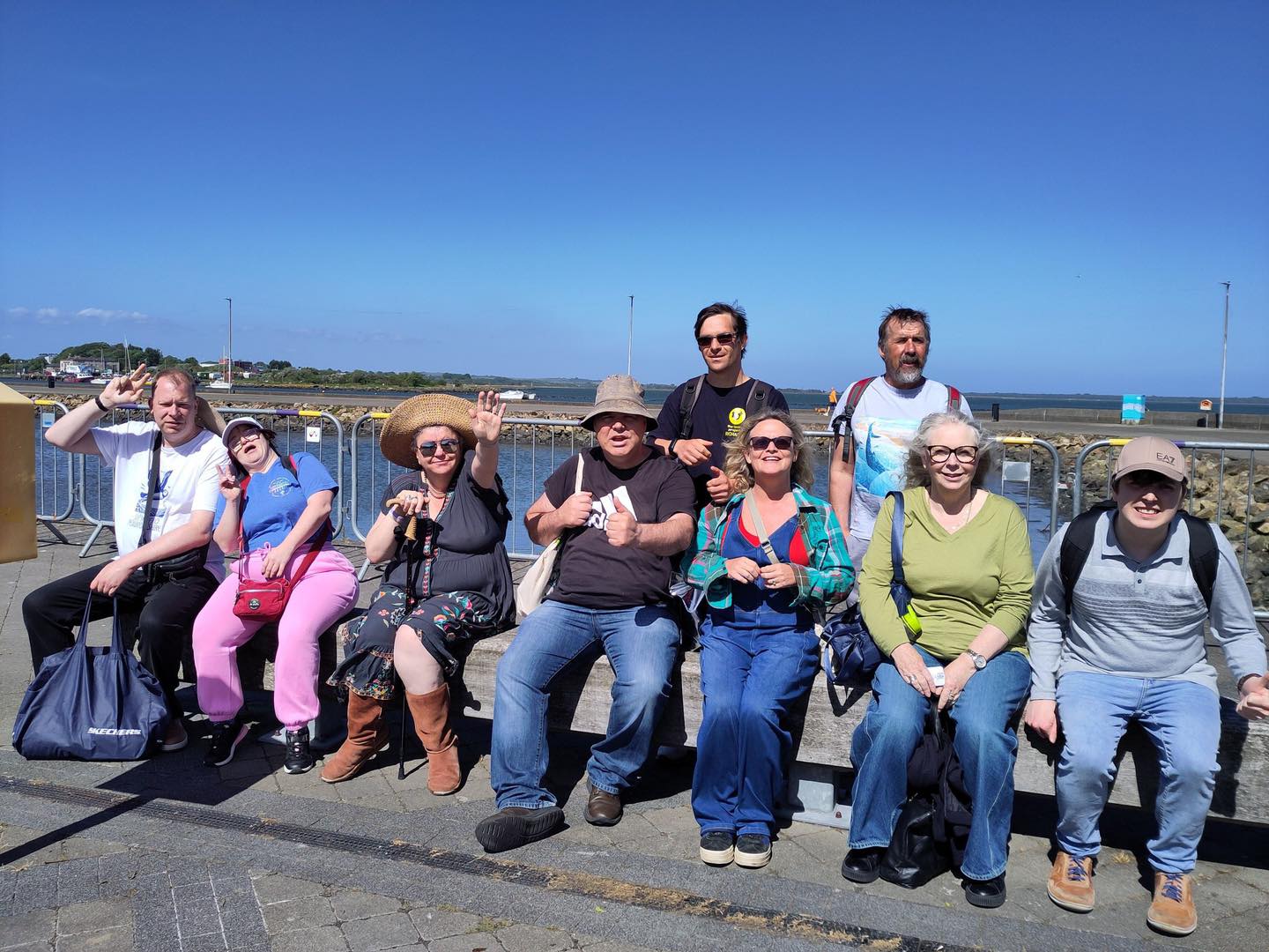 Grŵp o gyfranogwyr o The Tenby Project CIC yn eistedd gyda'i gilydd ar bromenâd glan dŵr yn Iwerddon yn ystod eu hymweliad dysgu rhyngwladol