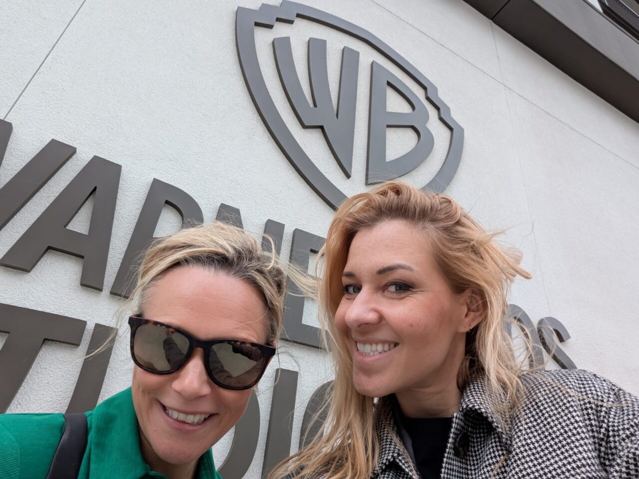 Mae Marlen Komorowski a Sara Pepper yn sefyll o flaen logo Warner Bros. Studios.